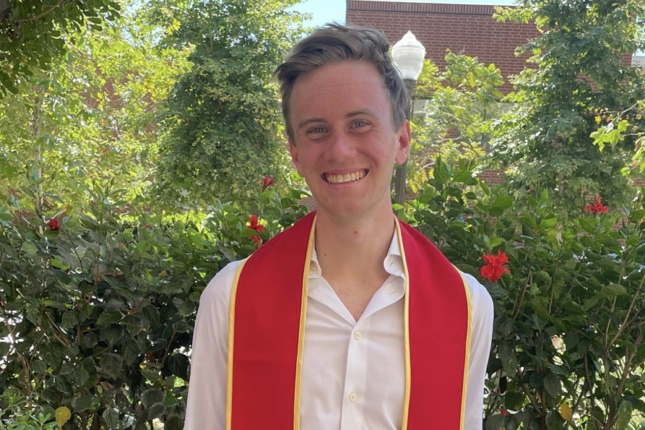 male presenting person with red graduation stripes in front of greenery
