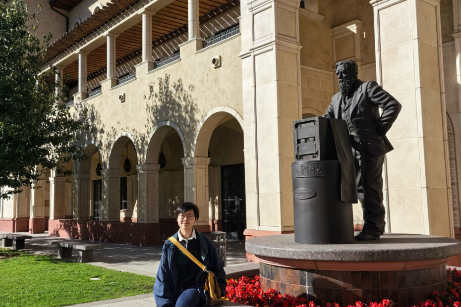 Person sitting on the ledge of a sculpture in an open courtyard of a building